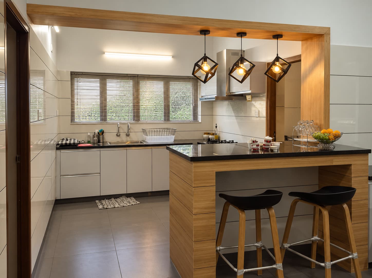 The kitchen at Dr. Faris Residence, with pale cabinetry, a timber breakfast counter and geometric pendant lights